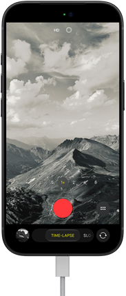 iPhone 18 Pro, front exterior, displaying a mountainous landscape, with the camera mode overlay in Time-Lapse mode, with power cable attached to charging port